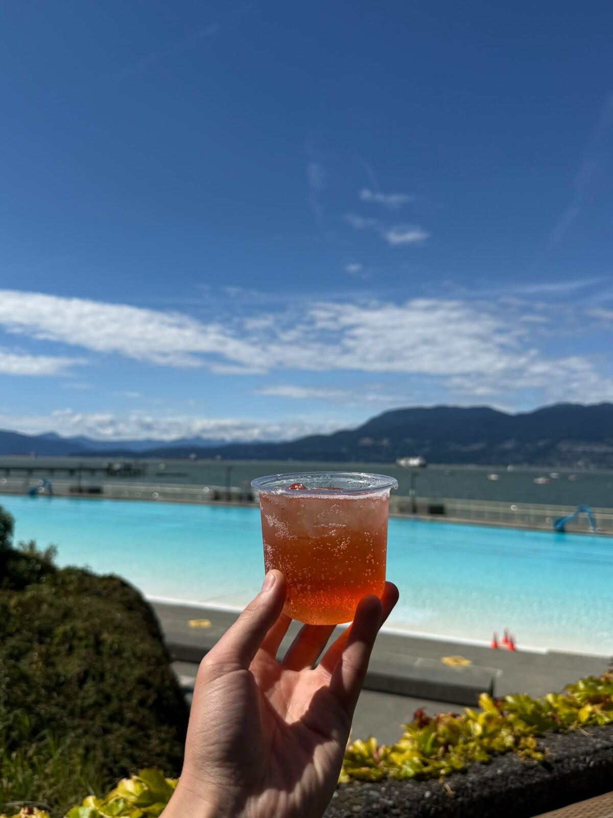 A Sprizzini held up in front of Kitsilano pool and the North Shore mountains