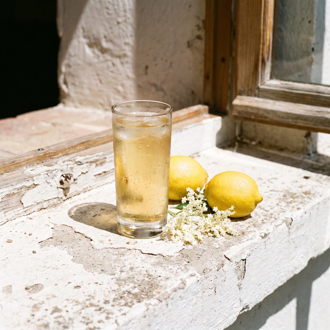 A Limoncello Spritz on a whitewashed sill in full sun with lemons and elderflower