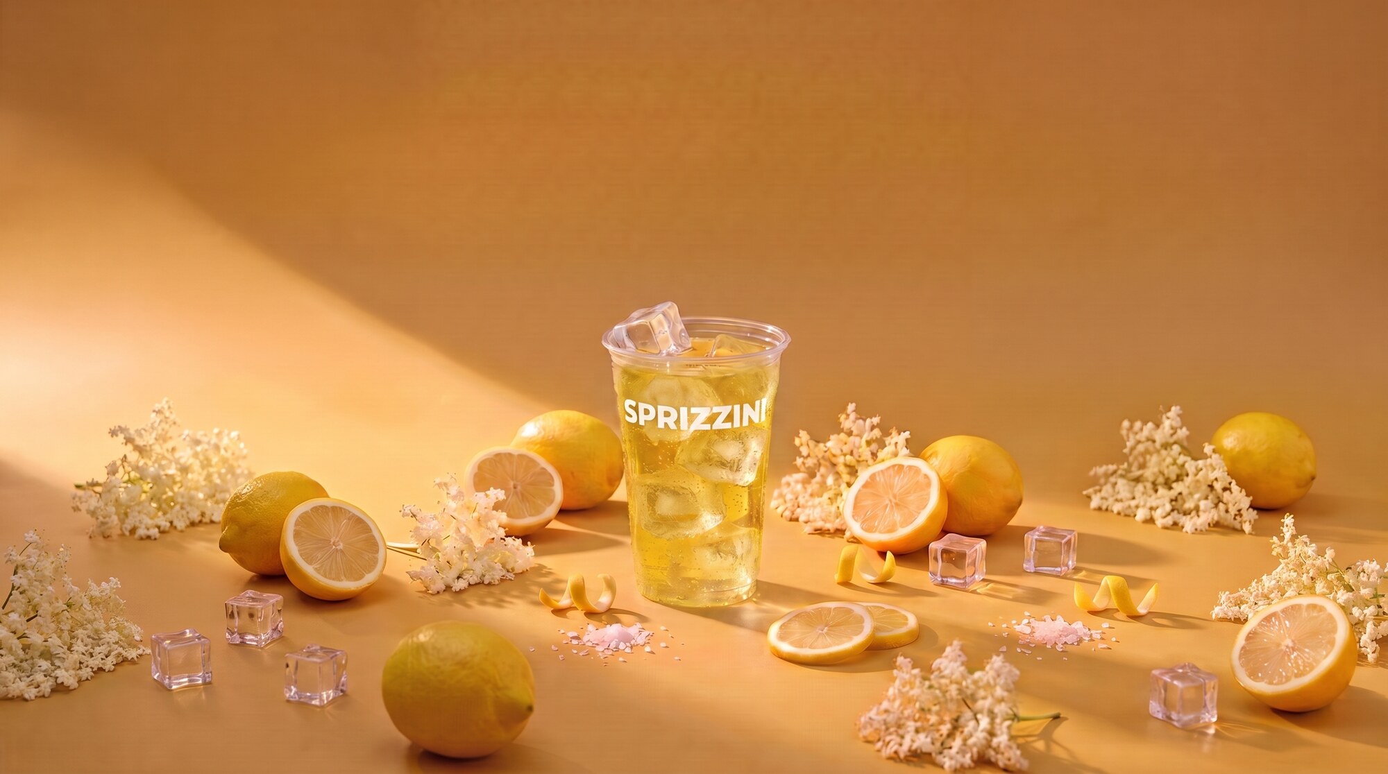 A Limoncello Spritz in a branded Sprizzini cup on a golden studio set, lemons and elderflower around it