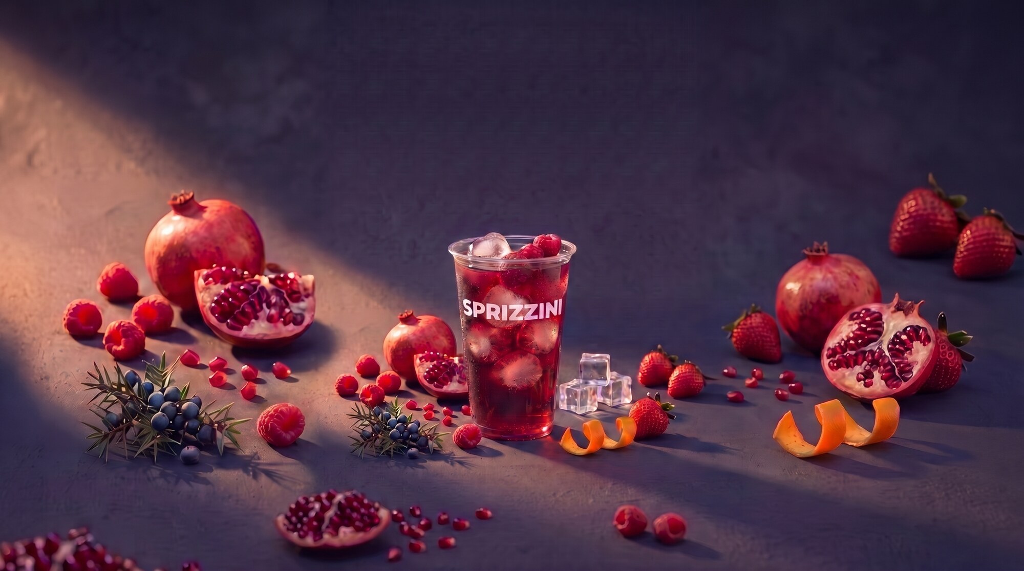 A Raspberry and Pomegranate Spritz in a branded Sprizzini cup on a dark slate studio set, pomegranate and raspberries around it